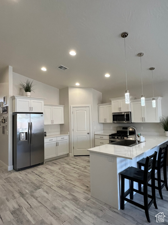 Kitchen featuring light wood-type flooring, white cabinets, sink, pendant lighting, and appliances with stainless steel finishes