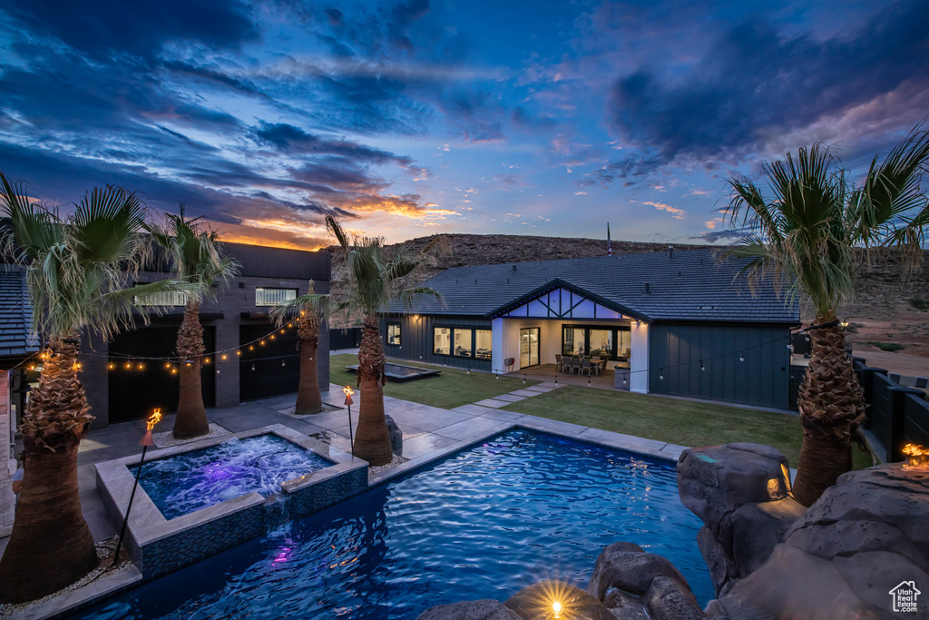 Pool at dusk with an in ground hot tub, a patio area, a lawn, and pool water feature