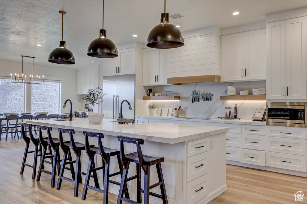 Kitchen featuring a center island with sink, an inviting chandelier, and white cabinetry