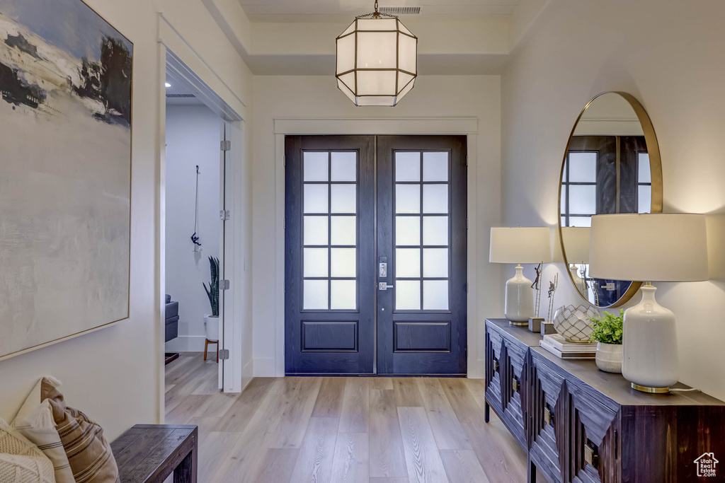 Doorway to outside with light hardwood / wood-style floors, a raised ceiling, a wealth of natural light, and french doors