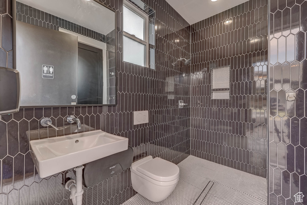 Bathroom featuring tiled shower, tile walls, sink, toilet, and tile flooring