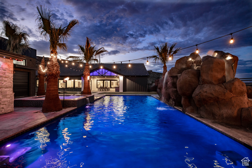 Pool at dusk with pool water feature and a patio area