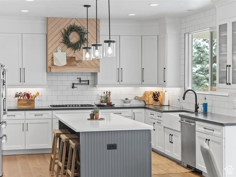 Kitchen with light hardwood / wood-style flooring, backsplash, a center island, pendant lighting, and appliances with stainless steel finishes