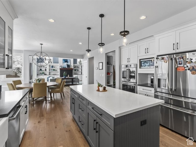Kitchen with light wood-type flooring, white cabinetry, an inviting chandelier, pendant lighting, and appliances with stainless steel finishes