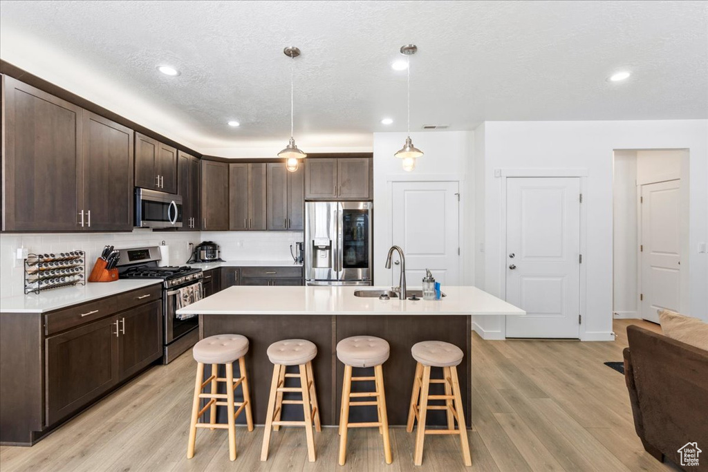 Kitchen featuring appliances with stainless steel finishes, light hardwood / wood-style floors, a breakfast bar, and decorative light fixtures