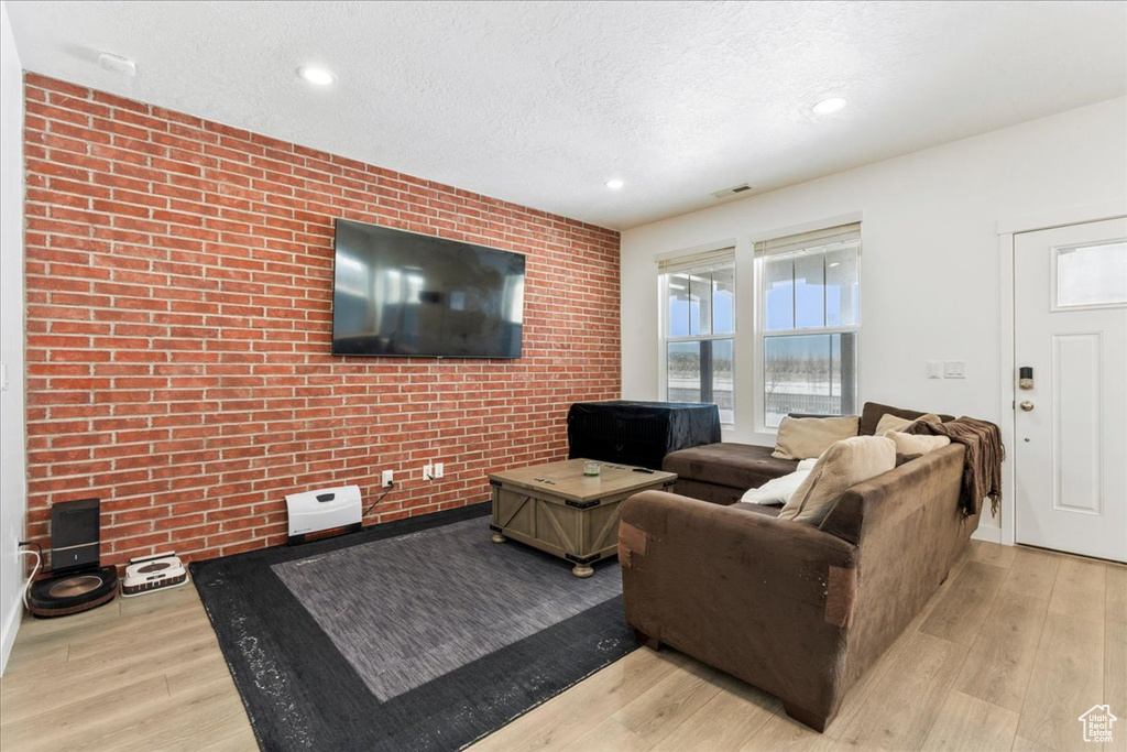 Living room with light wood-type flooring, a textured ceiling, and brick wall