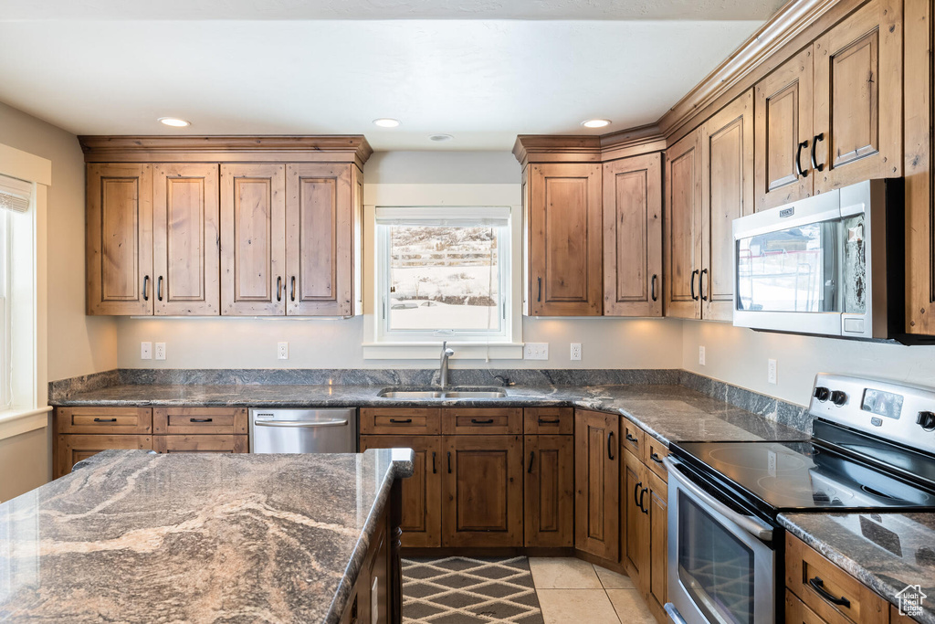 Kitchen featuring light tile flooring, appliances with stainless steel finishes, dark stone countertops, and sink