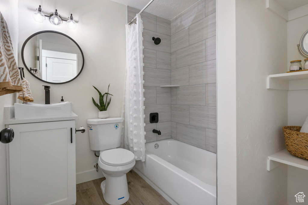 Full bathroom with shower / bathtub combination with curtain, a textured ceiling, vanity, hardwood / wood-style floors, and toilet