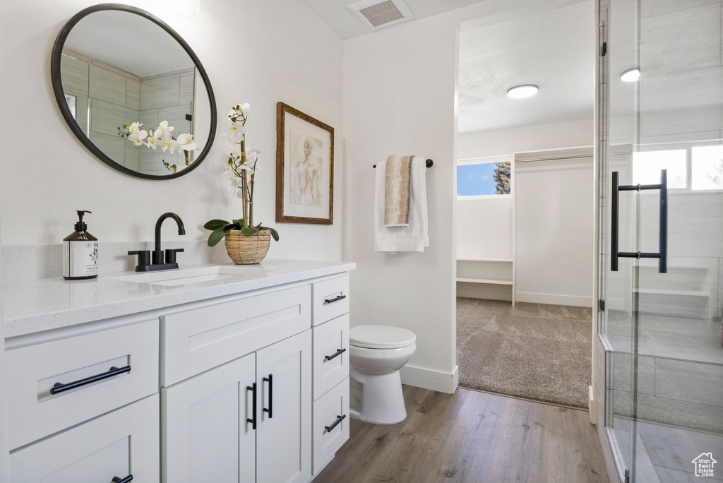 Bathroom featuring hardwood / wood-style flooring, vanity, walk in shower, and toilet