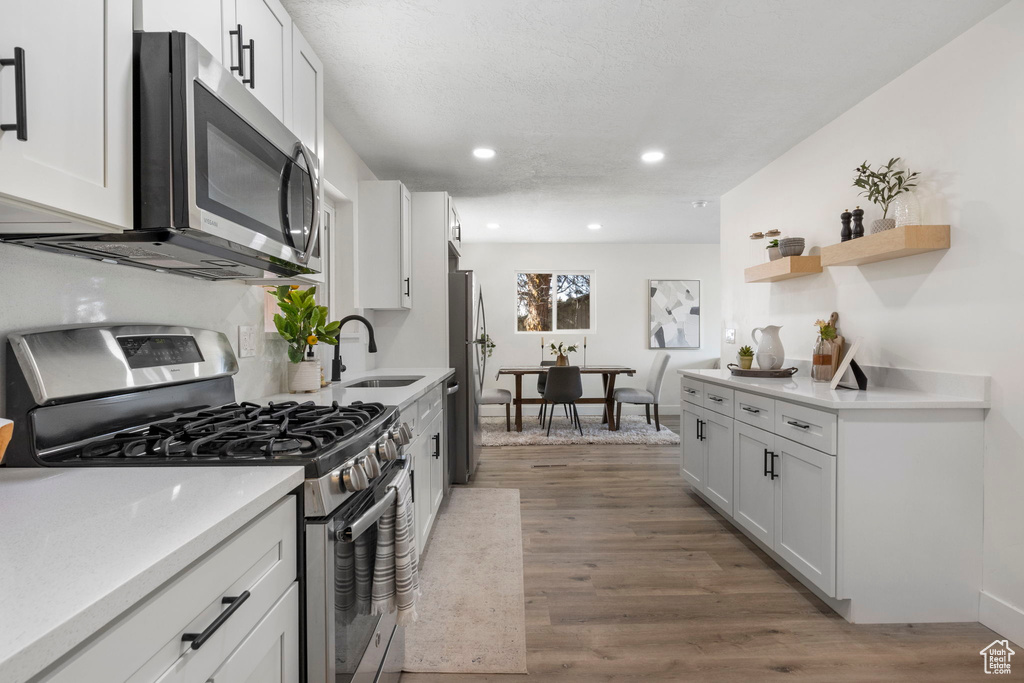 Kitchen with white cabinets, light hardwood / wood-style floors, sink, and appliances with stainless steel finishes