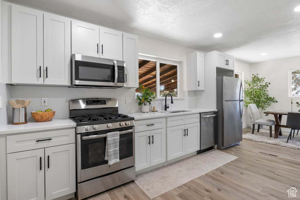 Kitchen with appliances with stainless steel finishes, light hardwood / wood-style flooring, a healthy amount of sunlight, and white cabinets