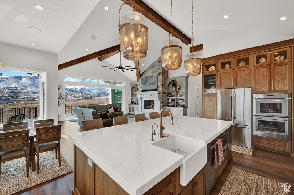 Kitchen with pendant lighting, dark wood-type flooring, appliances with stainless steel finishes, and a kitchen island with sink
