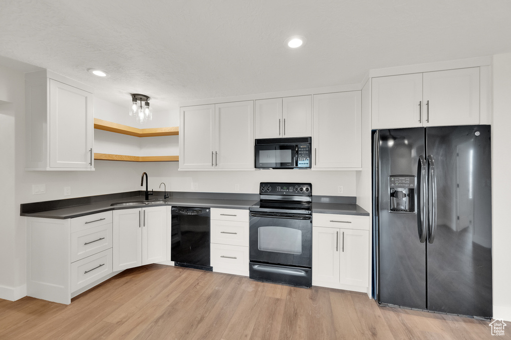 Kitchen with white cabinetry, light hardwood / wood-style floors, black appliances, and sink