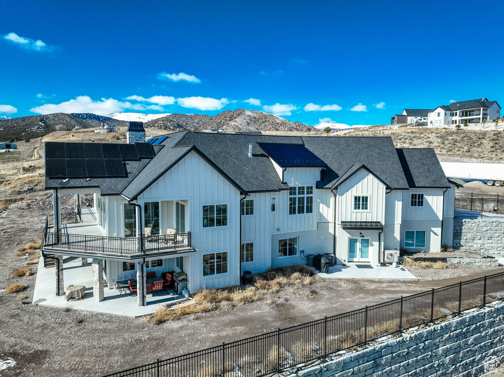 Snow covered rear of property featuring a mountain view, a balcony, a patio, and solar panels