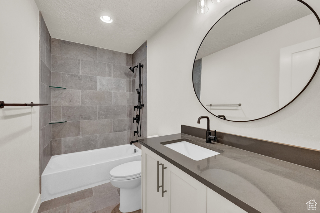 Full bathroom featuring large vanity, tiled shower / bath, a textured ceiling, toilet, and tile floors
