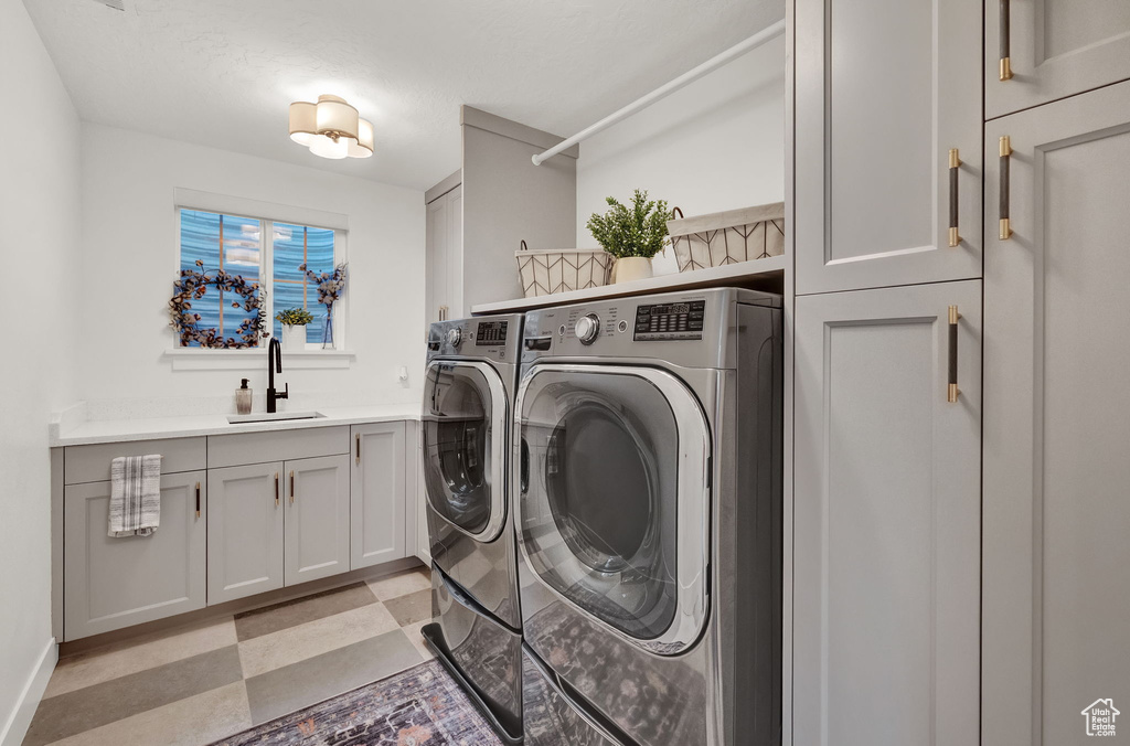 Clothes washing area featuring washing machine and clothes dryer, light tile floors, cabinets, and sink