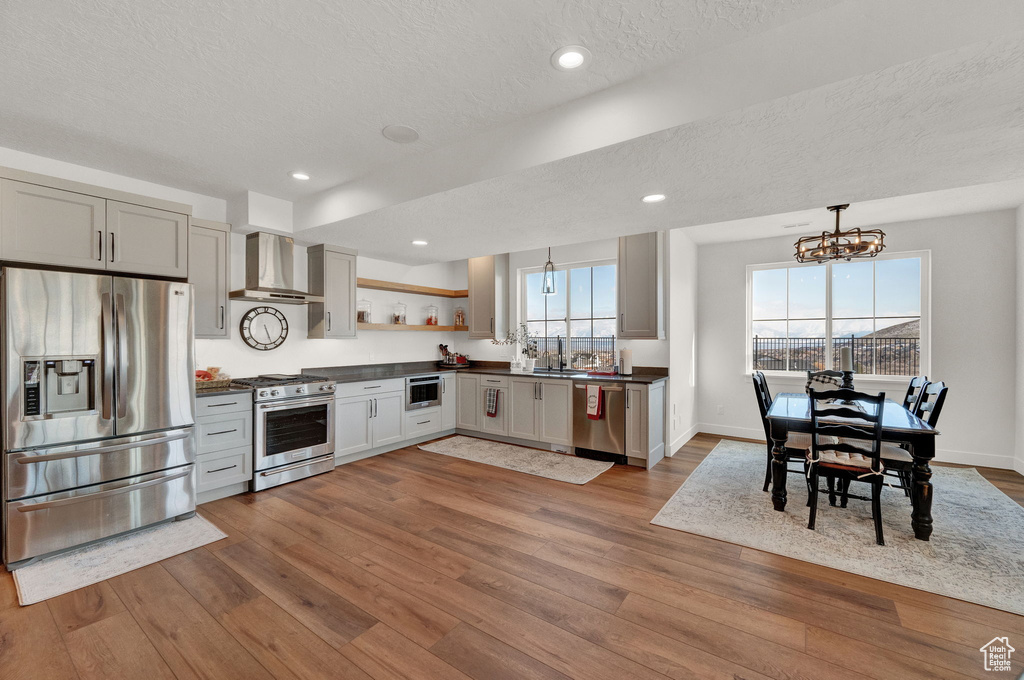 Kitchen featuring an inviting chandelier, stainless steel appliances, hanging light fixtures, wall chimney range hood, and wood-type flooring