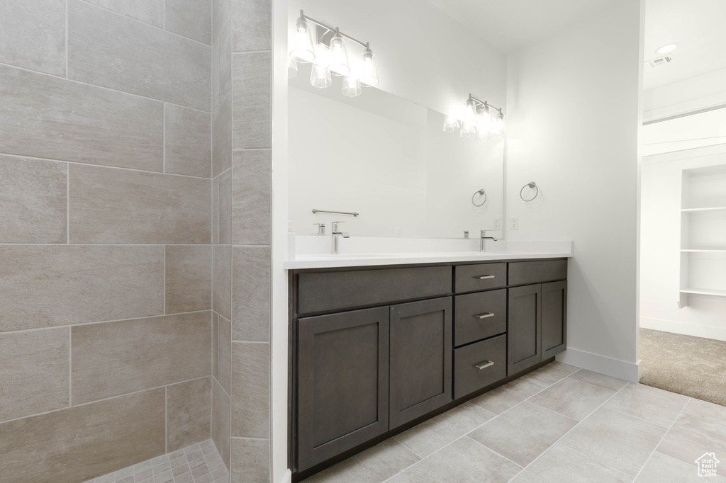 Bathroom featuring tile patterned flooring, vanity, and a tile shower