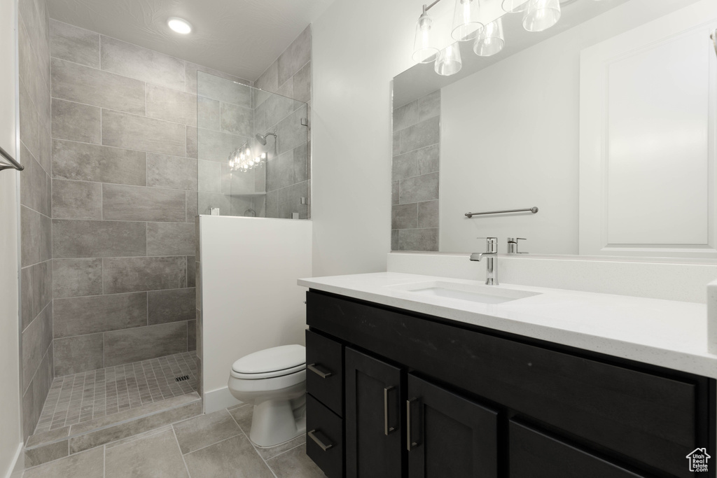 Bathroom featuring tile patterned flooring, vanity, toilet, and a tile shower