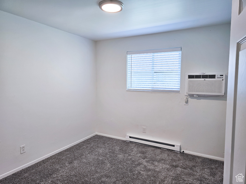 Empty room with a baseboard heating unit, carpet floors, and an AC wall unit
