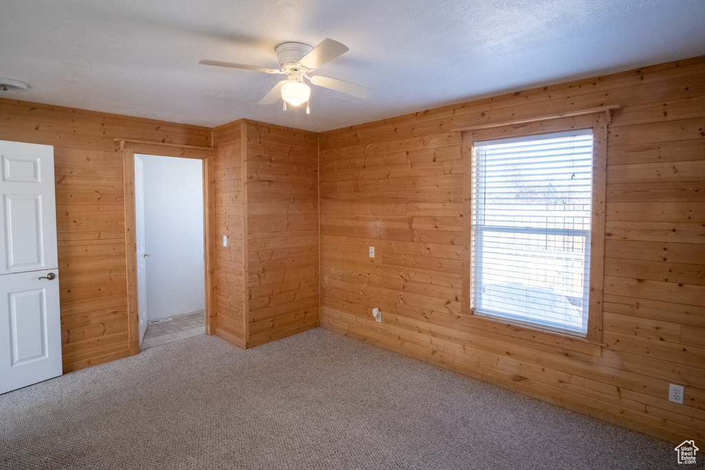 Unfurnished bedroom featuring wood walls, ceiling fan, and light carpet