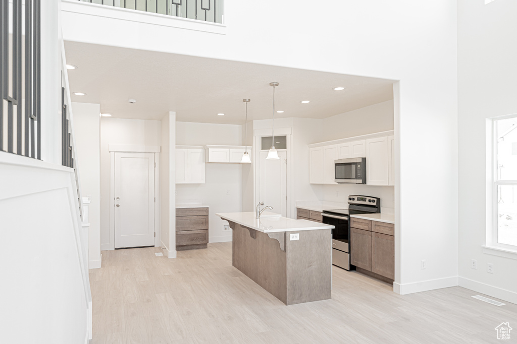 Kitchen featuring white cabinetry, a kitchen breakfast bar, decorative light fixtures, a center island with sink, and stainless steel appliances