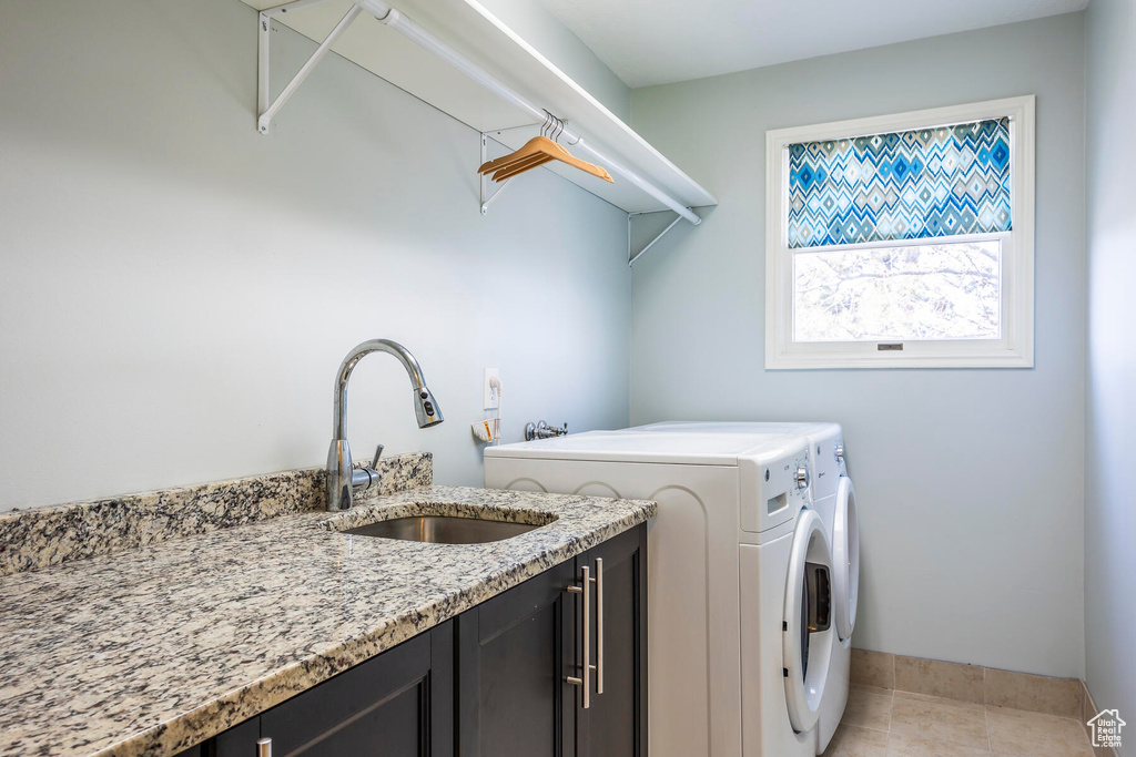 Clothes washing area with washer and clothes dryer, light tile floors, cabinets, and sink