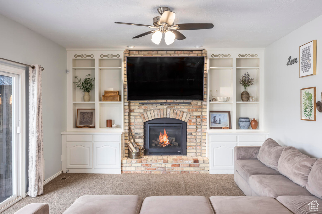Living room featuring a fireplace, ceiling fan, light carpet, and built in features