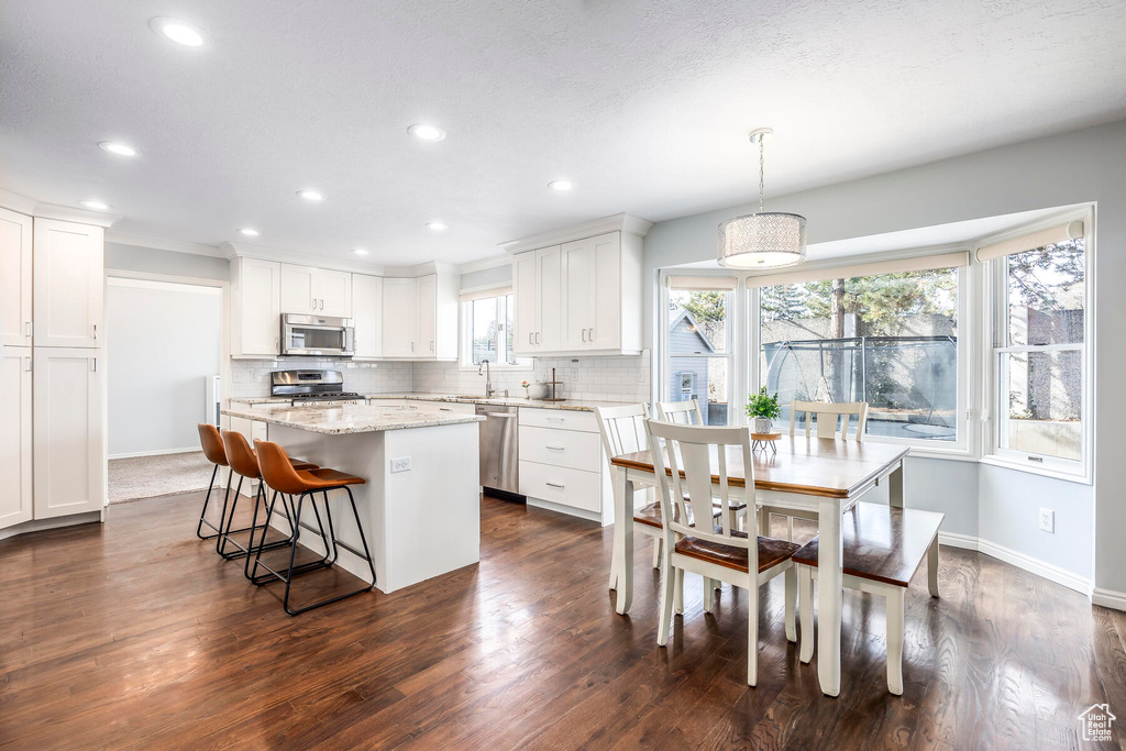 Kitchen featuring light stone countertops, tasteful backsplash, dark hardwood / wood-style floors, stainless steel appliances, and decorative light fixtures