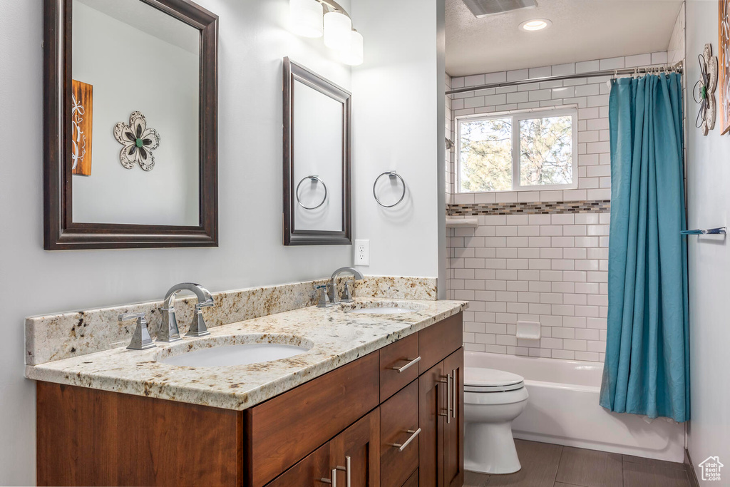 Full bathroom featuring dual sinks, shower / bath combo, oversized vanity, toilet, and tile flooring