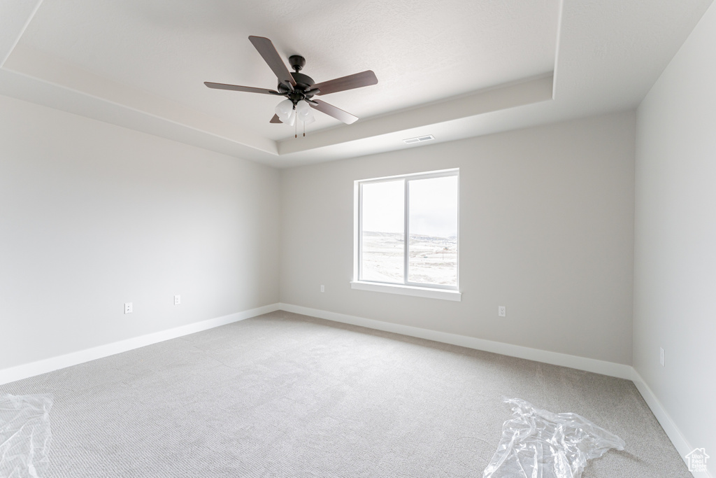 Spare room featuring light colored carpet, a tray ceiling, and ceiling fan