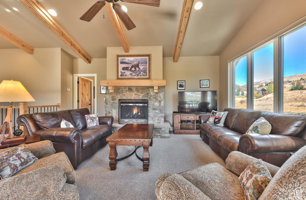 Living room featuring light carpet, ceiling fan, beam ceiling, and a stone fireplace