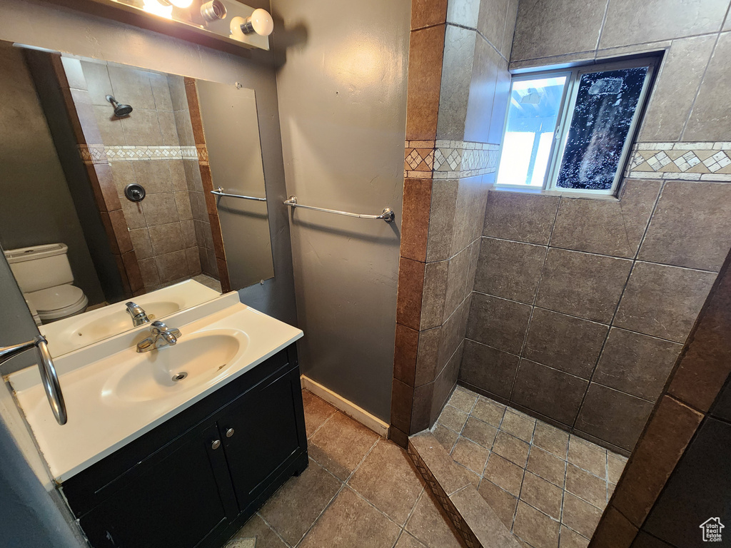 Bathroom featuring toilet, vanity with extensive cabinet space, tiled shower, and tile flooring