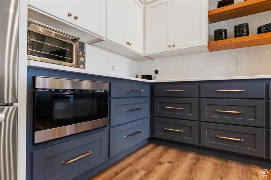 Kitchen featuring white cabinets, light hardwood / wood-style floors, stainless steel appliances, and tasteful backsplash