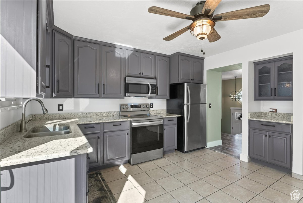 Kitchen with gray cabinets, stainless steel appliances, light stone counters, light tile flooring, and ceiling fan