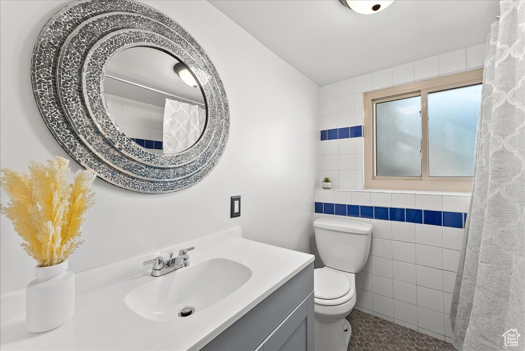 Bathroom featuring toilet, tile walls, vanity with extensive cabinet space, and tile floors