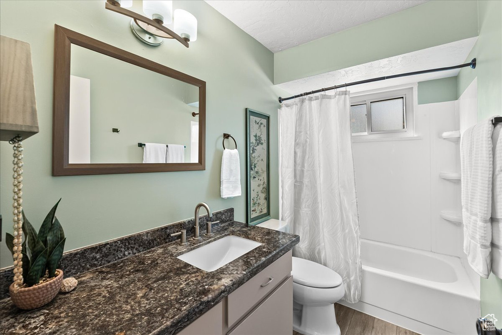 Full bathroom featuring a notable chandelier, shower / tub combo with curtain, a textured ceiling, toilet, and vanity with extensive cabinet space