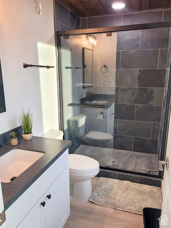 Bathroom featuring hardwood / wood-style floors, a shower with shower door, vanity, and toilet