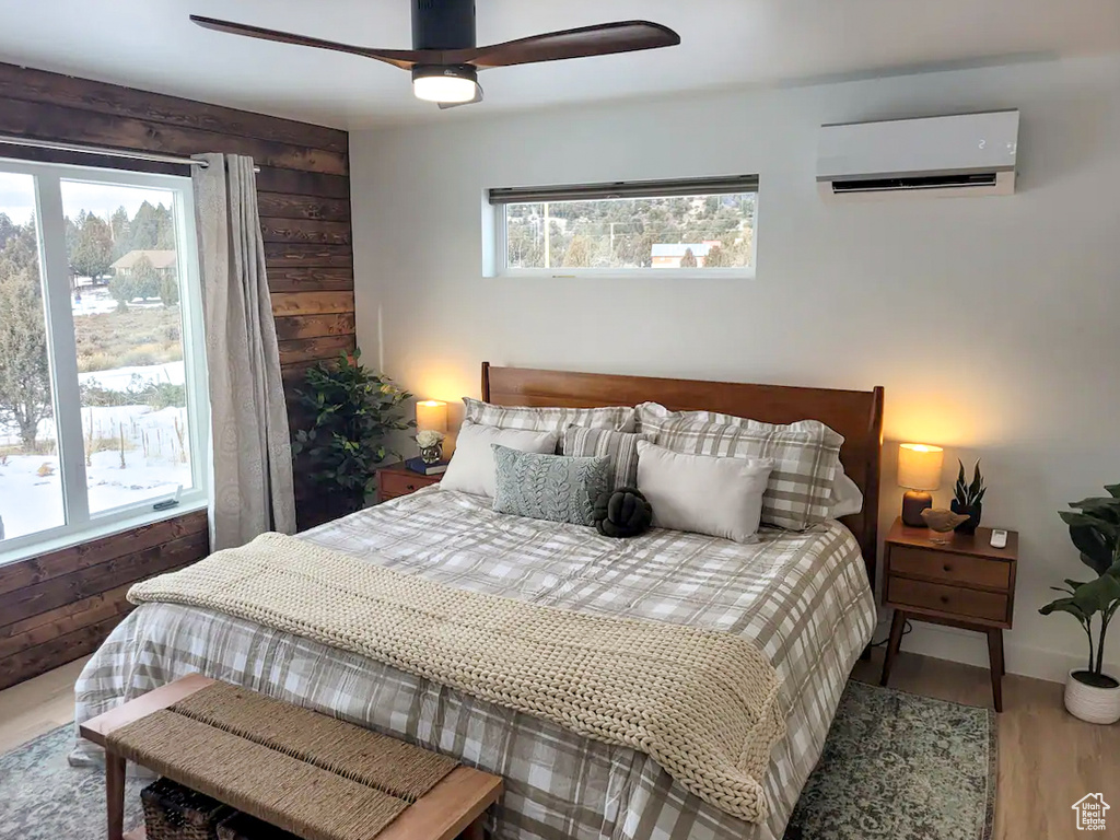 Bedroom with a wall mounted air conditioner, ceiling fan, wood walls, and wood-type flooring