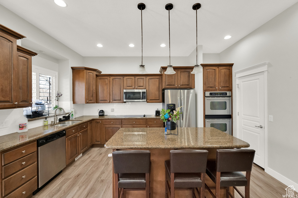 Kitchen featuring appliances with stainless steel finishes, light hardwood / wood-style flooring, a center island, and sink