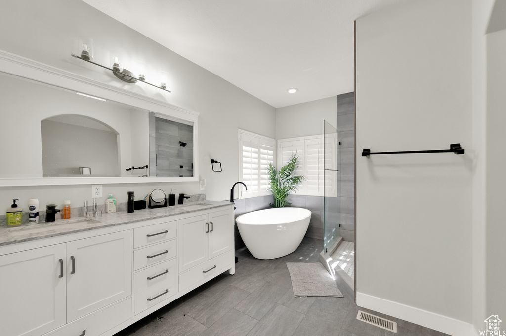 Bathroom featuring vanity with extensive cabinet space, shower with separate bathtub, double sink, and tile flooring