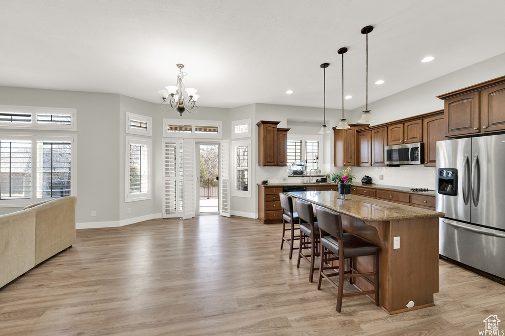 Kitchen with a chandelier, light wood-type flooring, stainless steel appliances, and decorative light fixtures