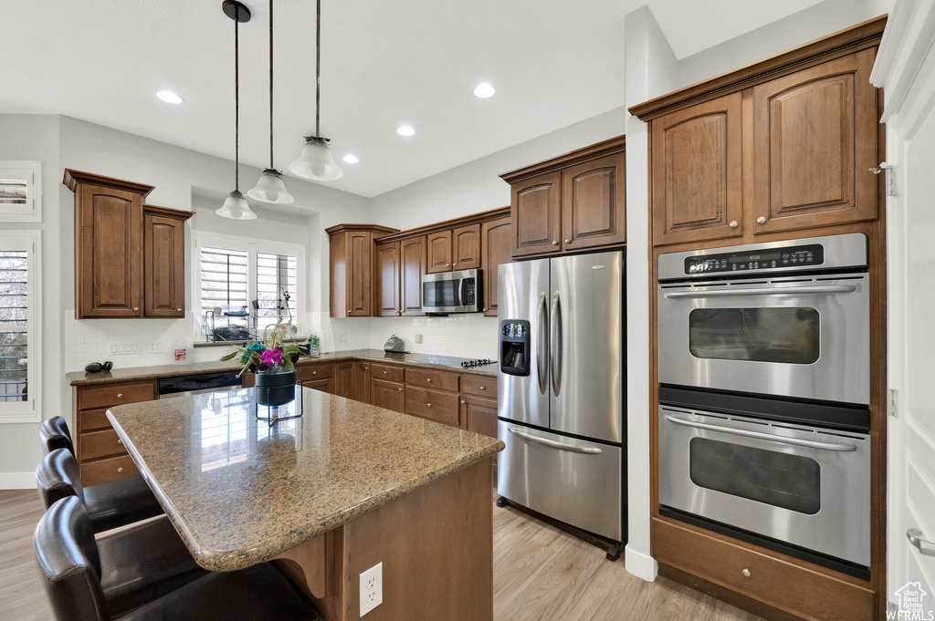 Kitchen with light hardwood / wood-style flooring, a center island, light stone countertops, a breakfast bar, and stainless steel appliances