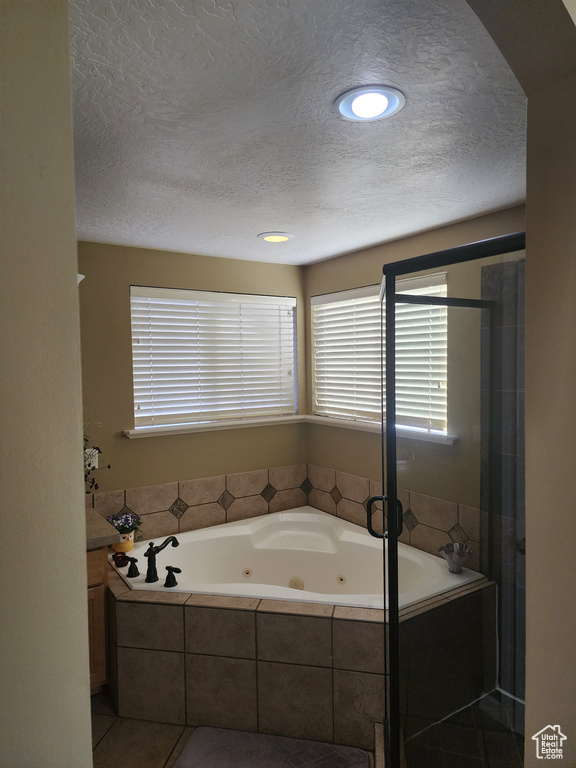 Bathroom with vanity, tiled bath, a textured ceiling, and tile flooring