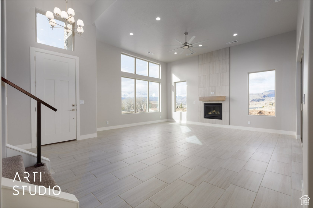 Unfurnished living room featuring ceiling fan with notable chandelier, a high ceiling, a tile fireplace, and light tile floors