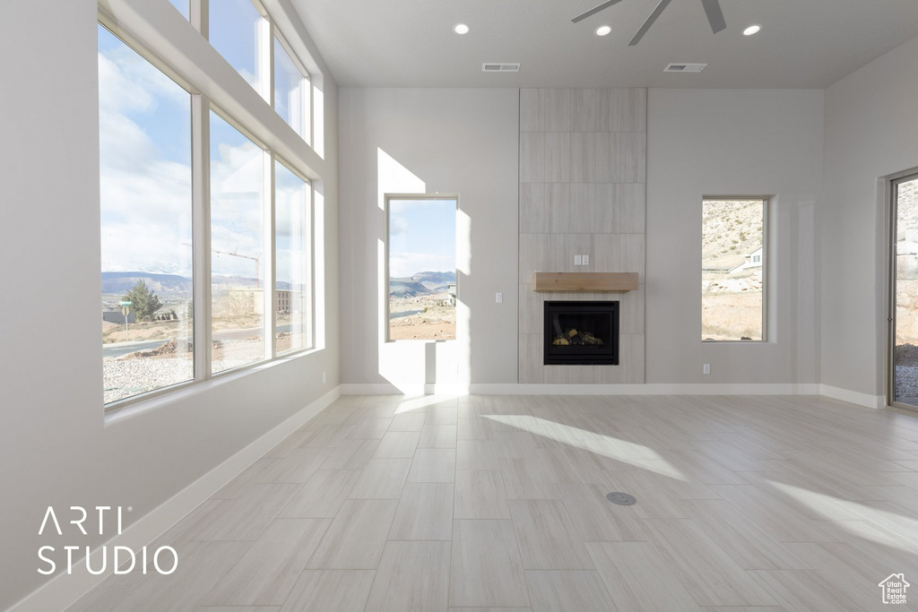 Unfurnished living room featuring plenty of natural light, ceiling fan, a fireplace, and light tile floors