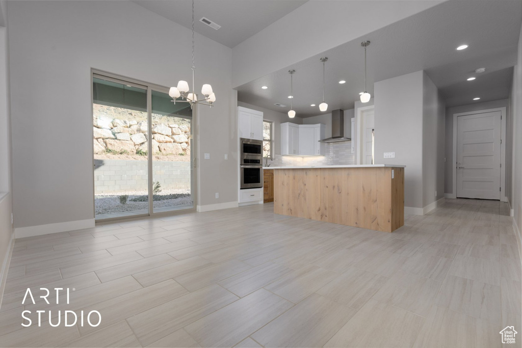 Kitchen with white cabinetry, an inviting chandelier, pendant lighting, and wall chimney range hood