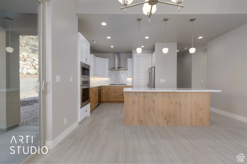 Kitchen with pendant lighting, white cabinetry, backsplash, appliances with stainless steel finishes, and wall chimney range hood