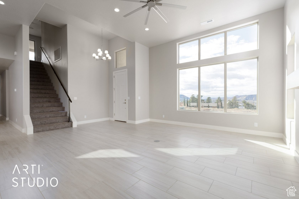 Unfurnished room featuring plenty of natural light, ceiling fan with notable chandelier, a towering ceiling, and light tile floors