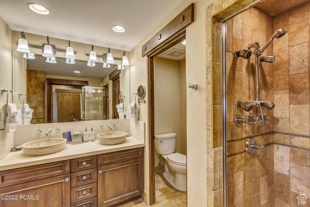 Bathroom with oversized vanity, walk in shower, double sink, toilet, and tile flooring